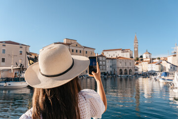 Female with a hat taking photos of the idyllic town of Piran, Slovenia