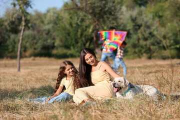 Poster - Little girl with her mother and cute dog resting on plaid outdoors