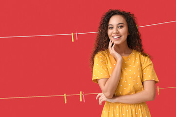 Wall Mural - Young African-American woman with hanging clothespins on red background