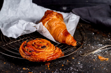 Poster - Closeup shot of a croissant and a cinnamon roll on a dark grey table