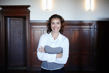 Wall Mural - Shes a positive influence in the courtroom. Cropped shot of an attractive female laywer standing with her arms folded and smiling widely in the courtroom.