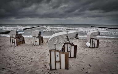 Sticker - Beautiful view of a sandy beach with wooden chairs against a dark gray dramatic sky