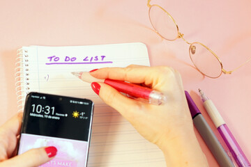 Wall Mural - Closeup shot of a woman holding a smartphone and writing down her 