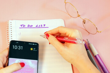 Wall Mural - Closeup shot of a woman holding a smartphone and writing down her 