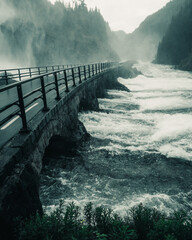 Sticker - Vertical shot of a bridge passing through a river and a waterfall flowing down from mountains