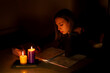 Young Caucasian woman studying by candlelight - blackout concept
