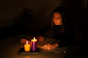 Wall Mural - Young Caucasian woman studying by candlelight - blackout concept