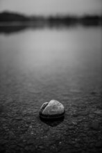 Grayscale Shot Of Pebbles On The Shore Of A Lake With A Blurry Background