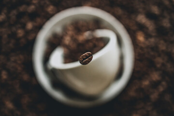 Poster - Selective focus of a roasted coffee bean falling into a cup on a blurry background