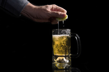 Wall Mural - Hand squeezing a lemon in a glass jar with refreshing beer on black background