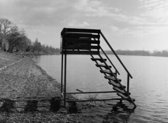 Sticker - Grayscale shot of an empty wooden tower over the lake under a cloudy sky