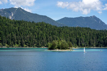 Sunny Summer View Of A Blue Lake With A Tiny Island And Mountains Nearby