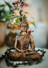 Canvas Print - Vertical shot of a brass Buddha statue with flowers in the background