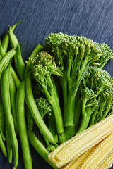 Wall Mural - Top view of broccolini, green beans and sweet corn on dark blue wooden table