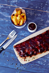 Wall Mural - Buffalo ribs, french fries and small white bowl of sauce with fork and knife on a wooden blue table