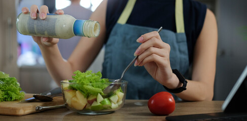 Young woman pouring salad dressing on salad in a glass bowl. Concept of healthy eating.