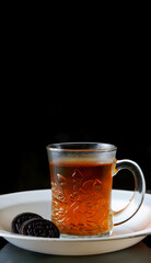 Poster - Vertical closeup of a cup of hot tea with cookies on a plate isolated on dark background