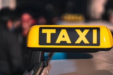 Poster - Shallow focus of a yellow TAXI sign on the top of a Taxi car with blurred people in the background