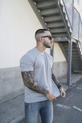 Canvas Print - Handsome Spanish man with tattoos wearing a gray t-shirt paired with sunglasses