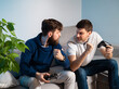 © phoenix021 - Two competitive man in their thirties playing video game console at home, fists in the air