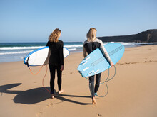 2 Caucasian Surfer Women On The Beach Walking To The Waves. They Are Wearing Winter Wetsuits.