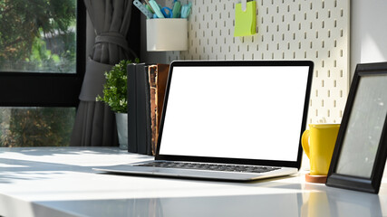 Mockup laptop computer with blank screen, picture frame and coffee cup on white table.