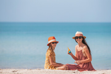 Wall Mural - Young mother applying sun cream to daughter nose on the beach. Sun protection