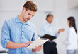 © Stigur/peopleimages.com - Young business man working on electronic tablet. Portrait of young business man working on electronic tablet with colleagues in background.