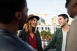 © StratfordProductions - Caucasian female laughing with group of multi-cultural friends socializing on a rooftop terrace at dusk.