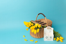 Intarnational Women Day. Wooden Calendar 8 Of March And Yellow Tulips In A Basket Of Vines On Blue Background. Copy Space