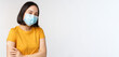 Covid-19, vaccination and healthcare concept. Cute asian girl in medical face mask, holding shoulder with band aid, got vaccine from coronavirus, smiling pleased, white background