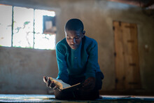 African Teenage Boy Sitting And Reading Book In Poor School, High Quality Photo