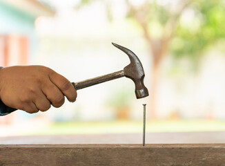 A carpenter hit a nails into an old wood stick in workshop.