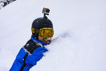 Smiling snowboarder with action camera lying in snow