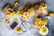 Overhead View Of Wrapped Gift Boxes, Dried Yellow Roses On A Table With Scissors And A Rustic Chalk Board Gift Tag