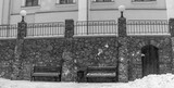 Fototapeta  - Black and white image of wooden benches with snow and ice. The seating area is directly in front of a stone wall.