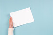 © vejaa - Female hands holding blank white paper sheet on light blue background. Top view. Mockup paper with copy space for text