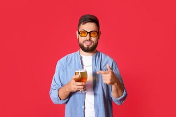 Sticker - Handsome man in sunglasses pointing at glass of beer on red background