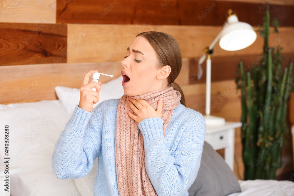 Ill young woman with sore throat using inhaler at home