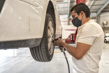 Latin Male Mechanic Removing A White Car's Wheel With An Impact Wrench
