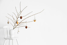 Vase With Tree Branches And Easter Eggs On Chair Near Light Wall
