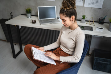 one woman young caucasian female sitting by the desk at work in the office study documents relaxing while hold clip chart with papers real people copy space female engineer or student planning project