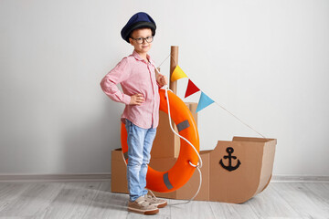 Poster - Funny little boy playing with cardboard ship and lifebuoy at home