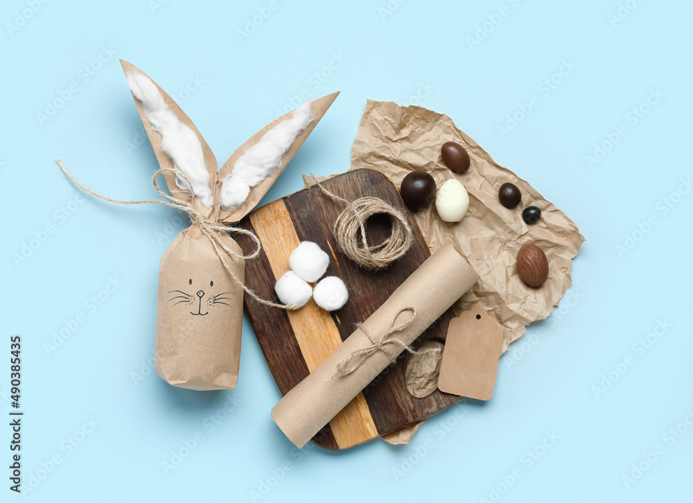 Composition with Easter bunny gift bag, chocolate candies, craft paper and rope on blue background