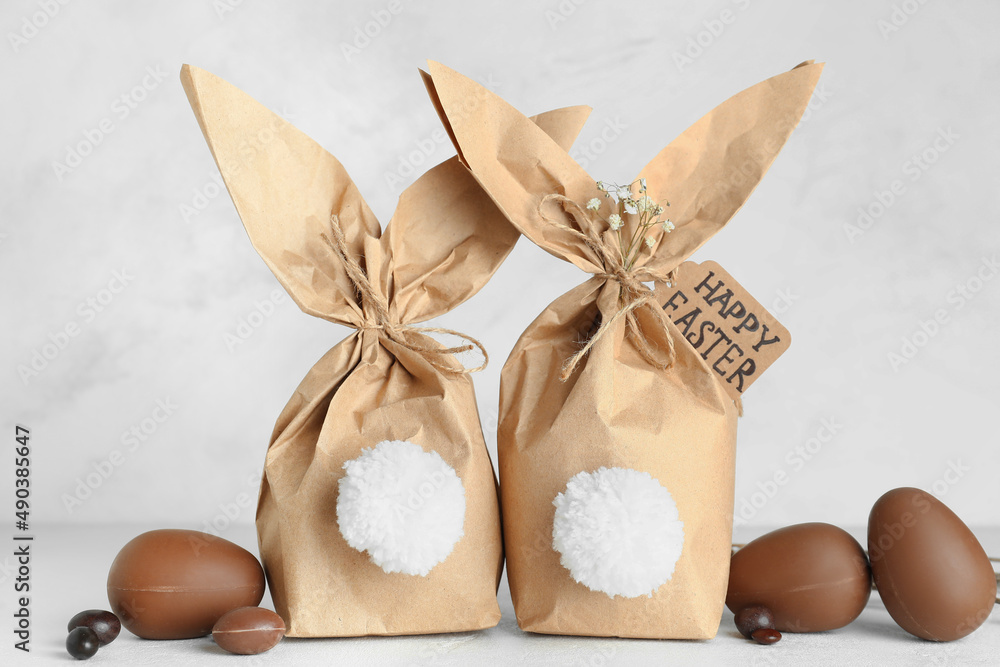 Easter bunny gift bags and sweet chocolate eggs on light background