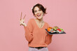 © ViDi Studio - Young smiling happy cheerful cool woman 20s in casual clothes hold in hand makizushi sushi roll served on black plate traditional japanese food chopsticks isolated on plain pastel pink background