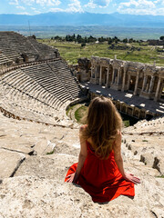 A young beautiful woman in a red dress walking in Pamukkale, Turkey, against the backdrop of the ruins of the ancient city of Hierapolis