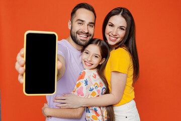 Wall Mural - Young happy parents mom dad with child kid daughter teen girl in basic t-shirts hold use mobile cell phone with blank screen workspace area isolated on yellow background studio. Family day concept