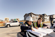 Female Engineers With Blueprints At Sunny Housing Development