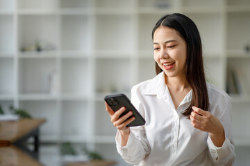 Portrait of a happy Asian businesswoman using mobile phone indoor, Asian businesswoman working in modern office.